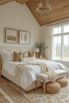 a large white bed sitting under a window next to a wooden ceiling with two pictures above it