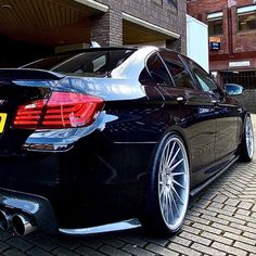 the rear end of a black car parked in front of a brick building on a cobblestone street