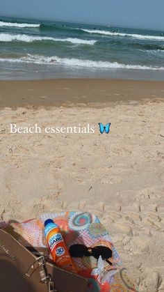 a beach towel, purse and sunglasses on the sand near an ocean with waves in the background