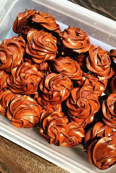 a plastic container filled with lots of chocolate covered doughnuts on top of a wooden table