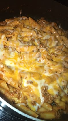 a skillet filled with cheesy pasta and meat covered in cheese on the stove