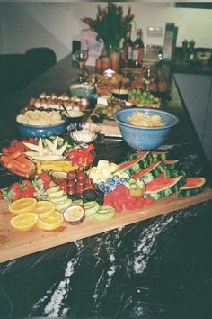 an assortment of fruits and vegetables on a wooden cutting board in front of a counter