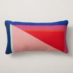 a pink, blue and red pillow on a white wall with an orange triangle in the middle