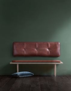 a brown leather bench sitting on top of a wooden floor next to a green wall