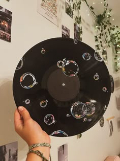 a person holding up a black record with bubbles on the disc and photos hanging above it