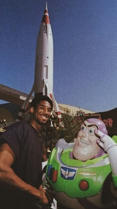 a man standing next to a giant toy buzz lightyear in front of a rocket ship