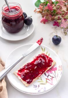 a piece of bread on a plate with jam in the jar and blueberries next to it