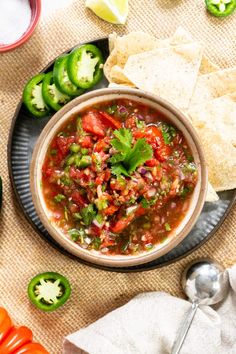 a bowl of salsa with tortilla chips on the side and green peppers around it