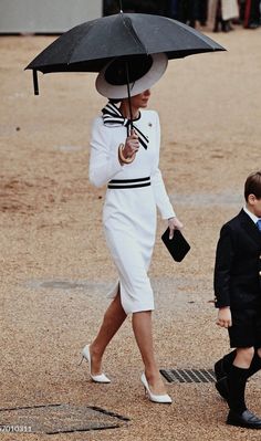 a woman in a white dress holding an umbrella and walking with a small boy on the other side