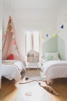 two beds in a room with pink and blue decor on the walls, white bedding and wooden floors