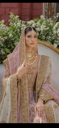 a woman sitting on top of a white couch wearing a pink and gold outfit with jewelry