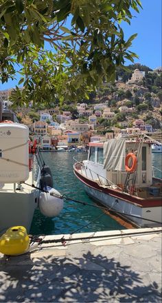 two boats are docked in the water next to each other near a hill with houses on it