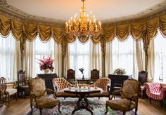 an elegant living room with chandelier, chairs, and table in front of large windows