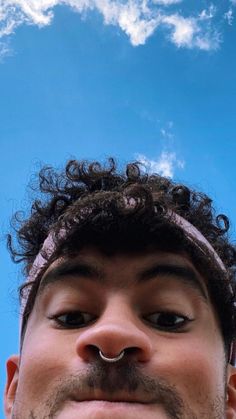 a man with curly hair and piercings on his nose looking up at the sky