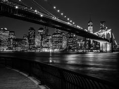 black and white photograph of the brooklyn bridge at night with city lights in the background