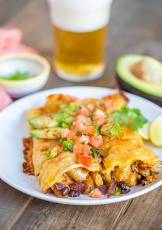 a white plate topped with food next to a glass of beer and an avocado