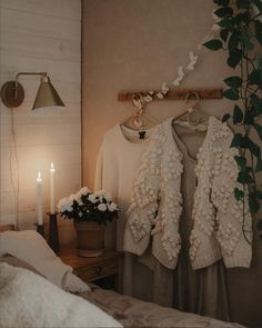 a white sweater hanging on a clothes rack next to a flower pot and two candles