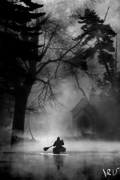 black and white photograph of a person in a canoe paddling through the water on a foggy day