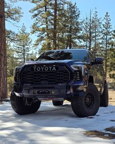 a black truck is parked in the snow near some trees and pine needles on a sunny day