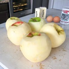 four apples sitting on top of a counter next to an egg carton and some eggs