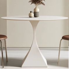 a white table with two chairs and a vase on it, in front of a wall