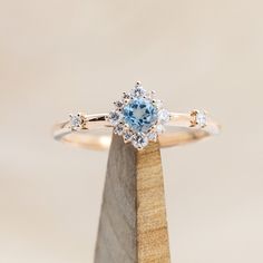 an engagement ring with a blue topazte surrounded by white diamonds on a wooden stand