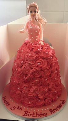 a barbie doll in a red dress on top of a birthday cake with pink frosting