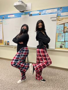 two women in plaid pants and black shirts standing next to a whiteboard with writing on it