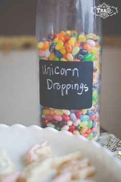 a glass jar filled with lots of colorful candies next to a sign that says unicorn droppings