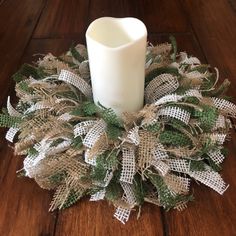 a white candle sitting on top of a wooden table next to a green and white wreath