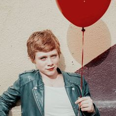 a boy holding a red balloon in front of a wall