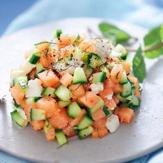 a salad with cucumbers, onions and herbs on a white plate next to green leaves