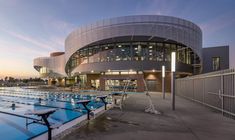 an empty swimming pool in front of a large building at dusk with people walking around