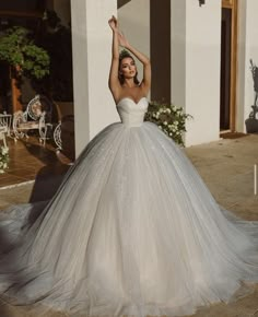 a woman in a wedding dress standing on the ground with her arms up and hands behind her head