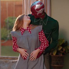 a man in a green suit kissing a woman wearing a red and white mask