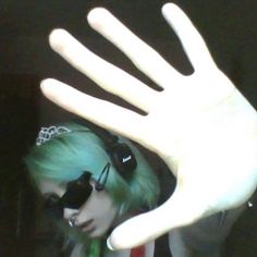 a woman with green hair wearing headphones and holding her hand up to the camera