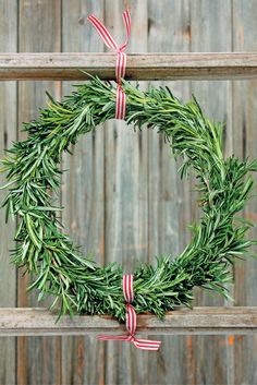 a green wreath with red and white ribbons hanging on a wooden fence