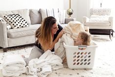 a mother and her daughter are playing in the laundry basket while sitting on the floor