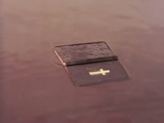 an old bible floating in the water with a cross on it's front cover