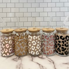 six glass jars with leopard print lids and straws in them on a marble countertop