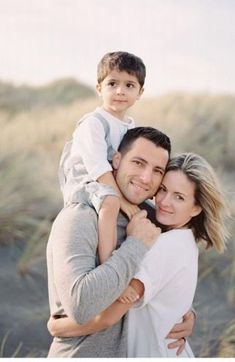 a man and woman holding a boy on their shoulders in the sand dunes at sunset