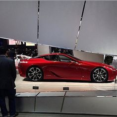 a man standing next to a red sports car on display in front of a mirror