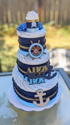 a three tiered cake is decorated with blue and white ribbons, an anchor, and the words ahoy boy on it