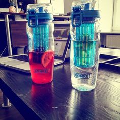 two water bottles sitting next to each other on top of a wooden table in front of a laptop computer