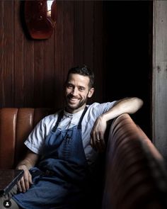 a man in an apron sitting on a leather couch with his arms crossed and looking at the camera