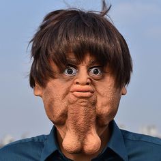 a man with his hands on his mouth is wearing a blue shirt and looking at the camera