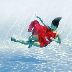 a woman floating in the water wearing a red dress