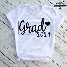 a white shirt with the word grad in black ink on it, sitting on top of a wooden floor