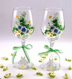 two wine glasses decorated with flowers and green ribbon tied around the rims, sitting next to each other