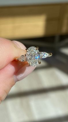 a woman's hand holding an engagement ring with three pear shaped diamonds on it